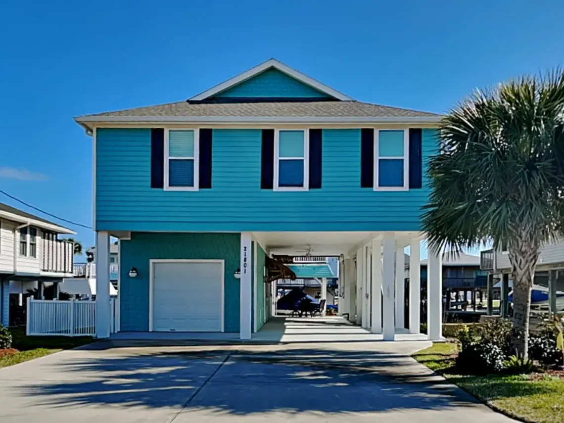 Tiki Retreat vacation rental in Galveston — turquoise stilt house with covered carport and palm trees